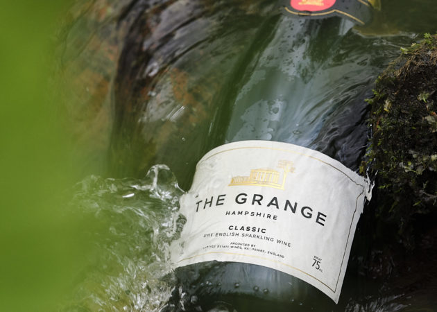 A bottle of The Grange CLASSIC English sparkling wine, partly submerged in a flowing stream of water